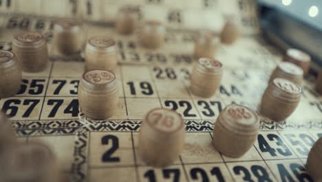 Macro-video-of-a-Bingo-board,-studio-lights,-120-fps,-slow-motion,-wooden-chip-digits,-Raw-footage,-lottery-desk-game,-card-numbers,-crane-pull-back-rotating-movement