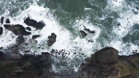 Vista-De-Arriba-Hacia-Abajo-De-Las-Olas-Del-Océano-Rompiendo-Contra-Las-Rocas-A-Lo-Largo-De-La-Costa-Rocosa,-La-Costa-De-Oregon-Del-Pulgar-De-Dios,-Toma-Aérea-Estática