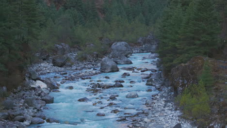 Drone-shot-of-blue-Dudh-Koshi-River-flowing-through-lush-green-forest-in-Phakding,-Everest-Base-Camp-trek,-Nepal