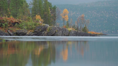 Rocky-banks-of-the-lake-covered-with-moss,-grass-and-colorful-autumn-trees