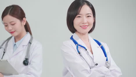 Medical-Hospital:-Two-female-doctors-young-eyewear-and-white-coats-discussing-patient-results-standing-in-white-coats-and-with-stethoscope-in-office