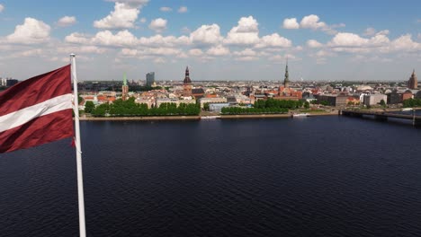 Beautiful-Aerial-View-Above-Riga,-Latvia-as-Latvian-Flag-Waves-in-Wind