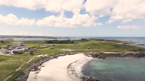 Flight-over-golden-beach,-headland-and-fields-on-north-coast-Guernsey-on-bright-sunny-day