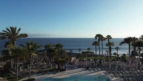 Aerial-view-of-a-coast-beach-flying-through-palms-and-swimming-pools-to-the-ocean-with-waves