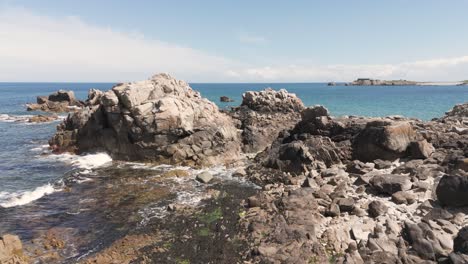 Waves-gently-washing-into-inlet-on-rocky-shoreline-on-bright-sunny-day-in-Guernsey-with-views-to-distant-headland