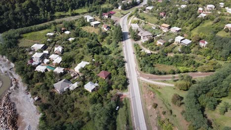 Draufsicht-Shooting-Eines-Autos,-Das-Durch-Das-Dorf-Auf-Der-Landstraße-In-Wunderschönen-Grünen-Wiesen-Und-Sonnigen-Bergen-Fährt