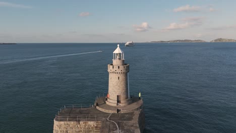 Reveal-of-lighthouse-and-breakwater-Castle-Cornet-St-Peter-Port,-Guernsey-with-cruise-ship-in-the-background-on-bright-sunny-day