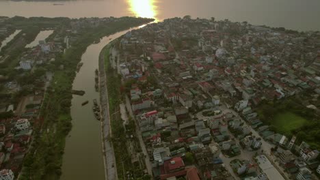 Aerial-view-of-Hanoi-at-sunset,-with-urban-sprawl-and-serene-river-reflecting-golden-light,-Vietnam