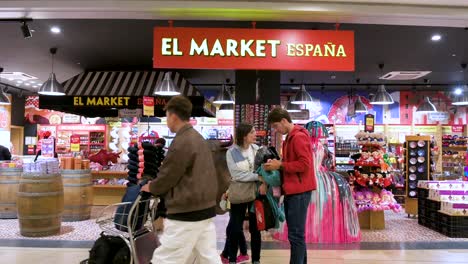 Passagiere-Sind-Vor-Einem-Spanischen-Souvenirladen-Zu-Sehen,-Der-Produkte-Mit-Spanischem-Thema-Am-Flughafen-Adolfo-Suárez-Madrid-Barajas-In-Madrid-Verkauft