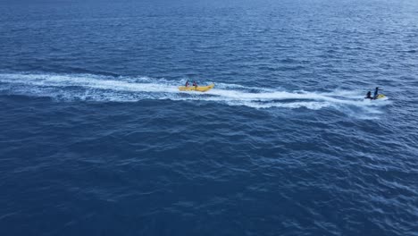 Young-Couple-on-Vacation-enjoying-Banana-Tube-Ride,-Drone-closeup-Follow