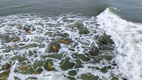 Crashing-white-foam-waves-on-rocks-in-beach,-slow-motion