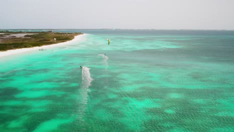 Kiteboarders-ride-over-clear-turquoise-waters-near-a-white-sandy-beach