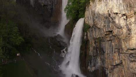 Seerenbach-Falls-cascading-down-a-steep,-rugged-cliff-surrounded-by-lush-greenery-and-mist-in-Amden,-Betlis,-near-Walensee,-Switzerland