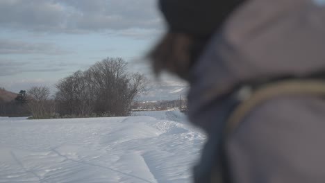 Person-in-a-jacket-looks-out-at-snowy-landscape-in-Hokkaido,-Japan-near-Iwanai-and-Niseko