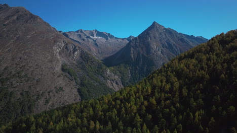 Saas-Fee-Saastal-aerial-drone-Switzerland-beautiful-sunny-blue-sky-autumn-fall-yellow-Larchs-forest-trees-Swiss-Alps-alpine-mountain-top-glacier-glacial-peak-gondola-tram-chairlift-landscape-forward