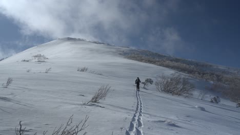 Snowboarder-ascending-snowy-slope-in-Iwanai,-Hokkaido-under-a-bright-blue-sky