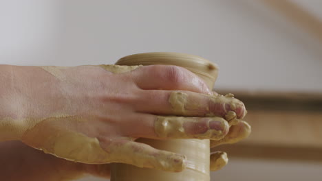 Handheld-close-up-shot-of-a-spinning-unfinished-case-on-a-potters-wheel,-caucasian-female-hands-working-with-the-vase,-forming-the-final-form