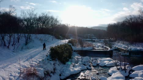 Snowy-landscape-with-a-person-walking-along-a-river-in-Iwanai,-Hokkaido,-Japan-at-sunrise