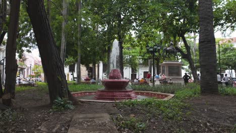 Pan-shot-of-water-fountain-surrounded-by-lush-vegetation-in-the-Bolivar-Square,-Cartagena