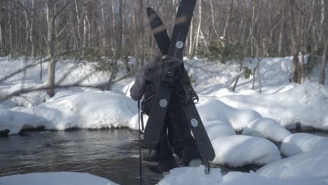 A-person-with-a-splitboard-crossing-a-snowy-stream-in-Hokkaido,-Japan