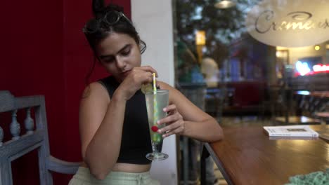 Mujer-Joven-Bebiendo-Una-Bebida-Verde-En-Un-Café-Al-Aire-Libre-En-Una-Tarde-De-Verano