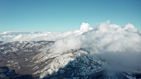 Snow-covered-mountains-with-fluffy-clouds-on-a-sunny-winter-day,-aerial-view