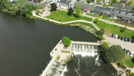 Dam-on-Rogue-River-in-Rockford,-Michigan-with-drone-video-overhead-and-then-tilting-up-to-city