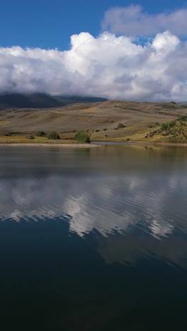 Vertikale-Luftaufnahme,-Blaues-Seewasser,-Grüne-Küste-Und-Flauschige-Wolken-An-Einem-Sonnigen-Sommertag