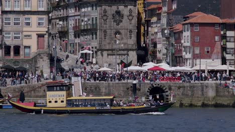 Porto's-riverside-and-river-with-boat-passing-and-people-walking-on-a-sunny-day