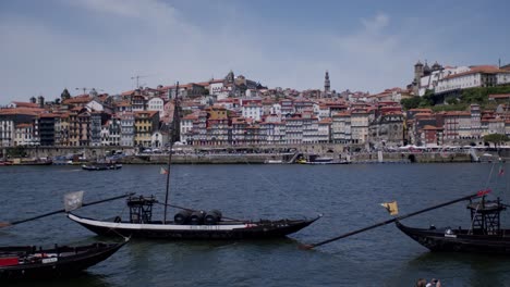 Traditionelle-Rebelo-Boote-Schwimmen-Im-Fluss-Douro,-Porto,-Mit-Dem-Flussufer-Im-Hintergrund-An-Einem-Sonnigen-Tag,-Weite-Aussicht