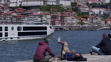 Menschen-Entspannen-Mit-Einem-Kreuzfahrtschiff-Im-Hintergrund,-Das-Auf-Dem-Fluss-Douro-In-Porto-Vorbeifährt