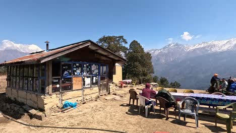 Vista-Sobre-Una-Idílica-Cabaña-De-Montaña-Con-Mesa-Para-Almorzar-En-Frente-Y-Excursionistas-Descansando-En-Frente