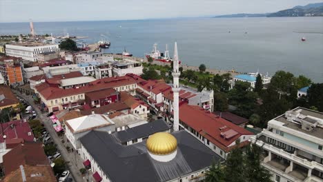 Aerial-shot-of-Batumi-Mosque-close-by-the-coast-of-the-black-sea-with-road-and-cars-passing-by-port