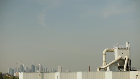 Industrial-rooftop-equipment-against-a-city-skyline,-showcasing-the-contrast-between-industry-and-urban-life