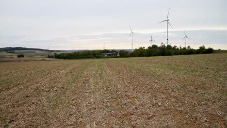 Abgeerntetes-Feld-Mit-Windturbinen-Unter-Einem-Bewölkten-Himmel,-Ländliche-Landschaft-Mit-Schwerpunkt-Auf-Nachhaltiger-Energie