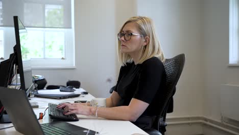 A-focused-woman-working-on-a-computer-in-a-bright,-modern-office-setting