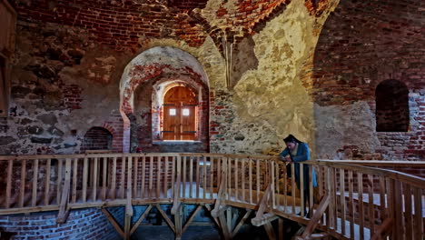 Toma-Panorámica-De-Una-Turista-Dentro-Del-Antiguo-Castillo-Medieval-De-Bauska-Con-Grandes-Ventanales-Y-Suelos-De-Madera-En-Letonia