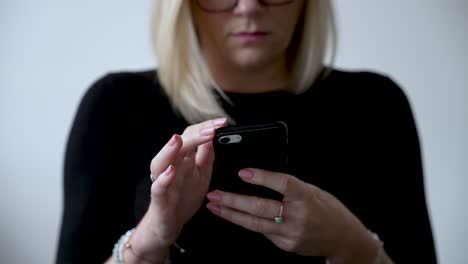 Blonde-Frau-Tippt-Auf-Einem-Smartphone,-Trägt-Eine-Brille,-Nahaufnahme,-Drinnen