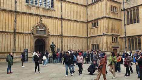 Busy-crowds-of-people-visiting-the-Bodleian-Library-main-research-library,-historical-tourism-landmark-and-attraction-of-University-of-Oxford,-England-UK