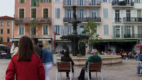 People-relax-by-fountain-in-Cannes-with-colorful-buildings-in-background