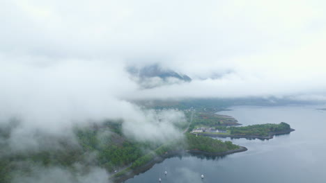 Neblige-Luftaufnahme-Von-Glencoe-In-Schottland-Mit-Wolken,-Die-Die-üppige-Landschaft-Und-Den-Ruhigen-See-Bedecken