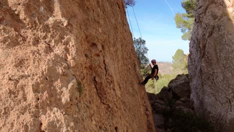 Man-rock-climbing-aerial-view-of-sportsman-rapelling-mountain-in-La-Panocha,-el-Valle-Murcia,-Spain-woman-rapel-down-a-mountain-climbing-a-big-rock