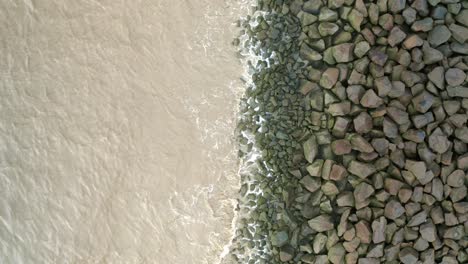 Sea-waves-hitting-rocks-on-a-sea-dyke,-drone-descending-overhead-shot