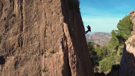 Man-rock-climbing-aerial-view-of-sportsman-rapelling-mountain-in-La-Panocha,-el-Valle-Murcia,-Spain-woman-rapel-down-a-mountain-climbing-a-big-rock