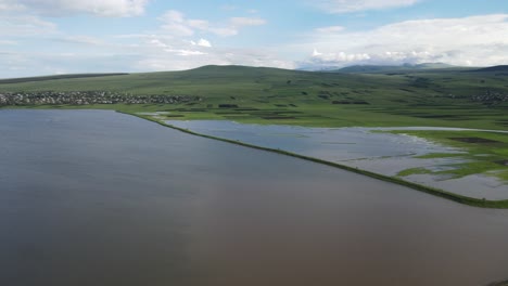 Aerial-shot-of-a-lake-surrounded-by-meadows-villages-old-houses-mountains