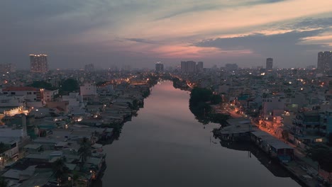 Evening-view-along-canal-in-Ho-Chi-Minh-City,-Vietnam-with-shanty-houses-illuminated-and-reflection-part-one