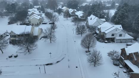 Aerial-view-of-a-suburban-neighborhood-covered-in-fresh-snow,-featuring-homes-and-bare-trees-under-a-cloudy-sky-in-the-USA