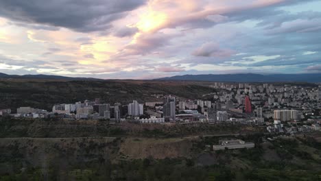 Aerial-shot-of-sunset-in-Tbilisi-Georgia-buildings-surrounded-by-mountains