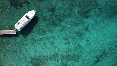 Yacht-moored-in-clear-blue-Lagoon-with-few-people-swimming-beside,-Drone-top-down