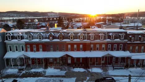 Golden-sunrise-over-a-row-of-historic-townhouses-covered-in-snow,-captured-from-above-by-a-drone-in-the-USA